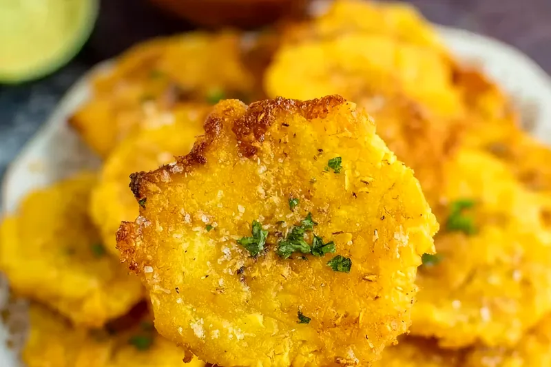 Green plantains, garlic, lime, salt, and oil arranged on a wooden cutting board with an air fryer in the background